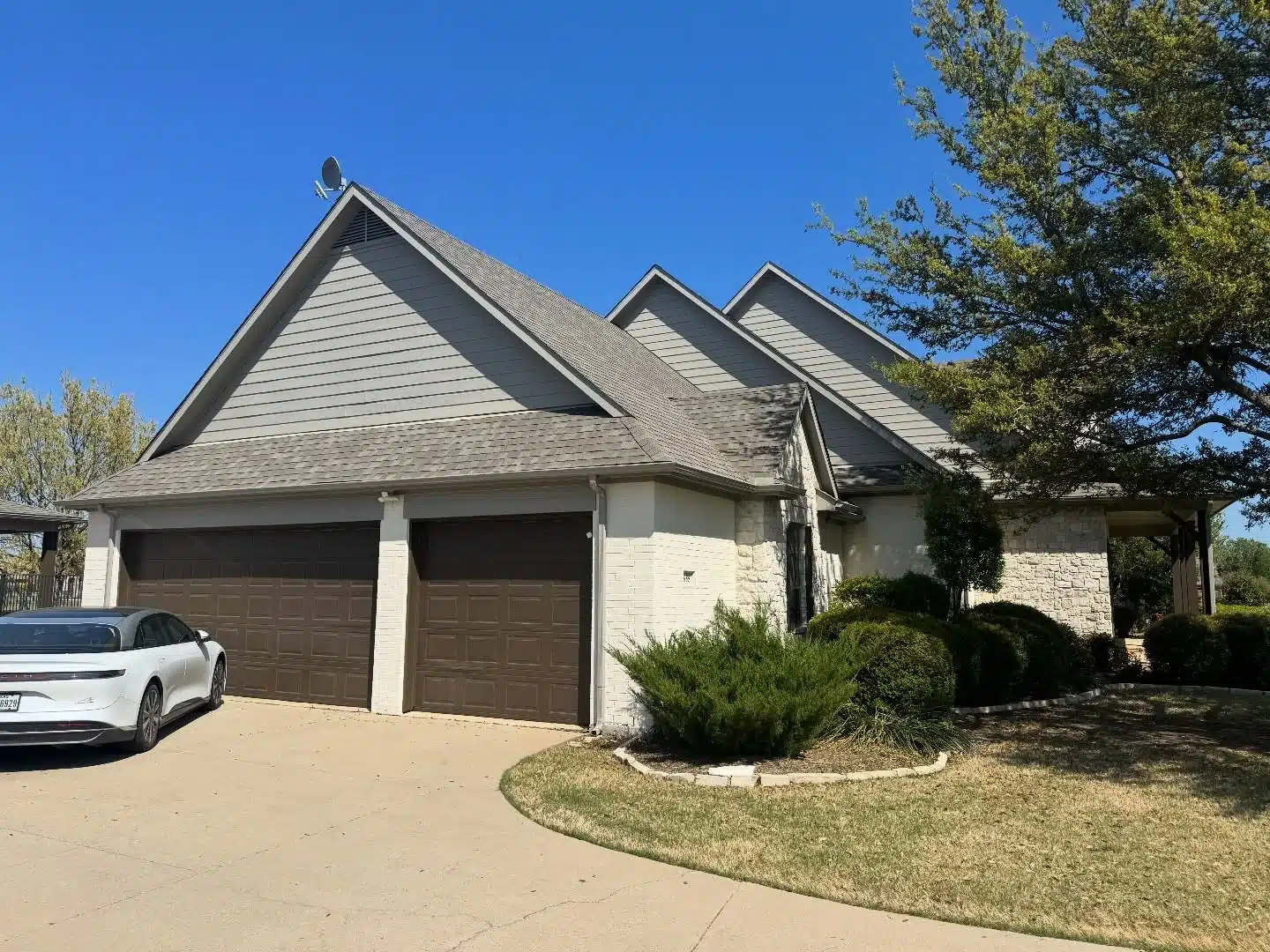 Expert garage door and exterior residential painting services Side view of a residential home showcasing freshly painted dark brown garage doors, white brick, and gray siding.